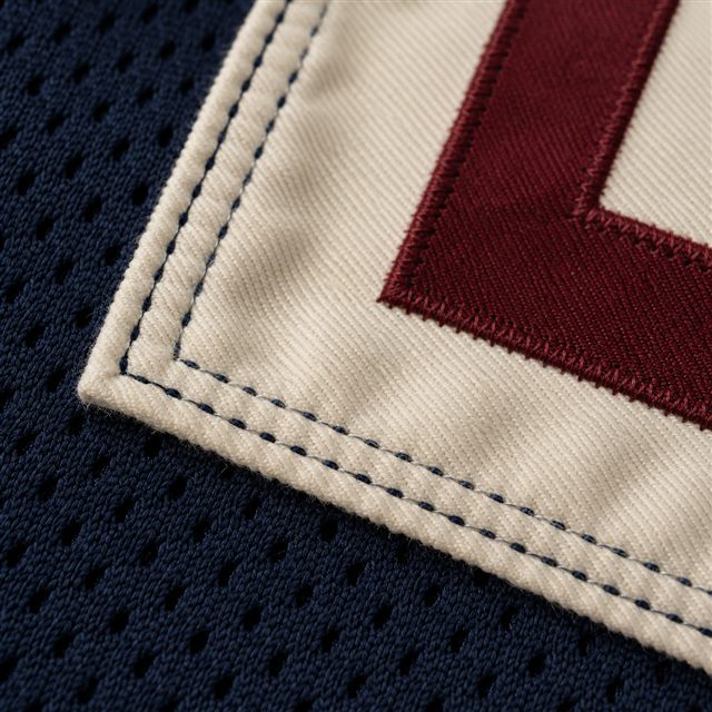 Parallel stitches securing an ivory nameplate to navy jersey fabric